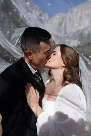 A romantic wedding photo showing a sweet kiss between newlyweds against a backdrop of snowy mountain peaks.