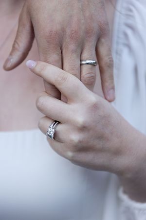 Close-up of elegant wedding rings being displayed on hands against a soft white background.