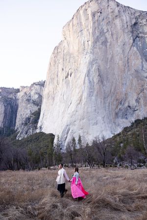 Two people stand in a meadow at Yosemite Valley with El Capitan's massive granite face towering in the background.