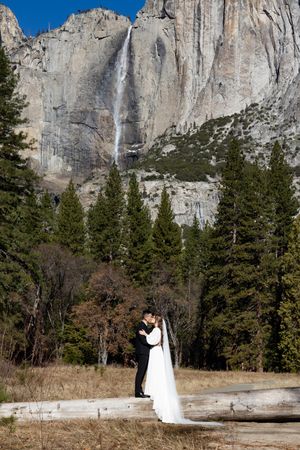 A couple shares an intimate moment against a backdrop of majestic Yosemite Falls and towering granite cliffs.