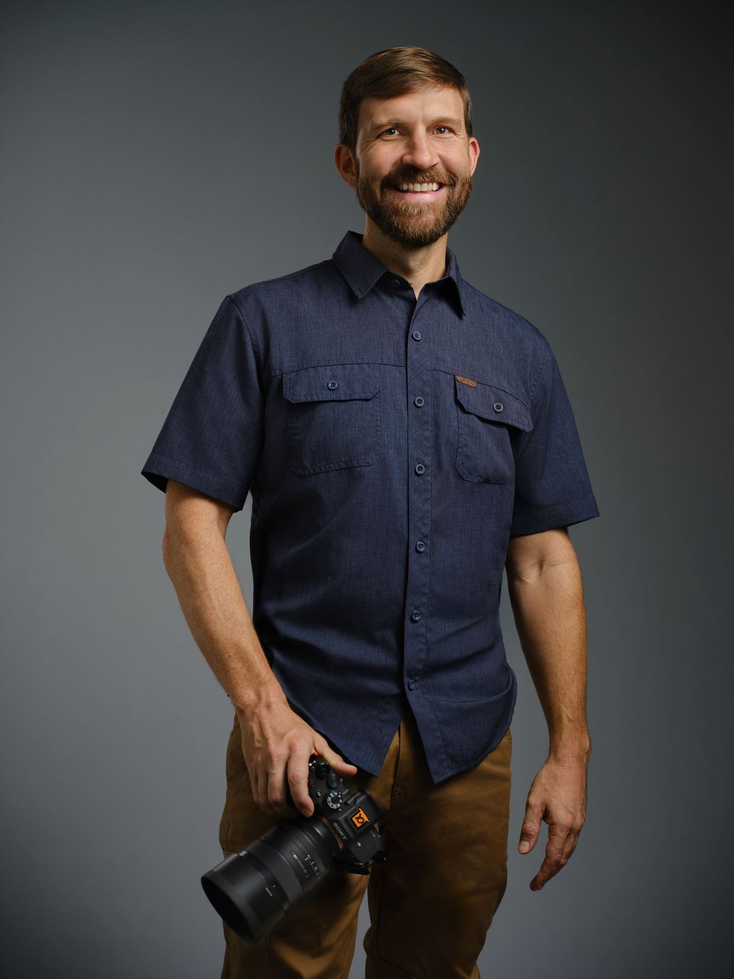 Alex Kent, Arkansas based commercial photographer, educator, and speaker with camera in hand crouches atop a bluff.