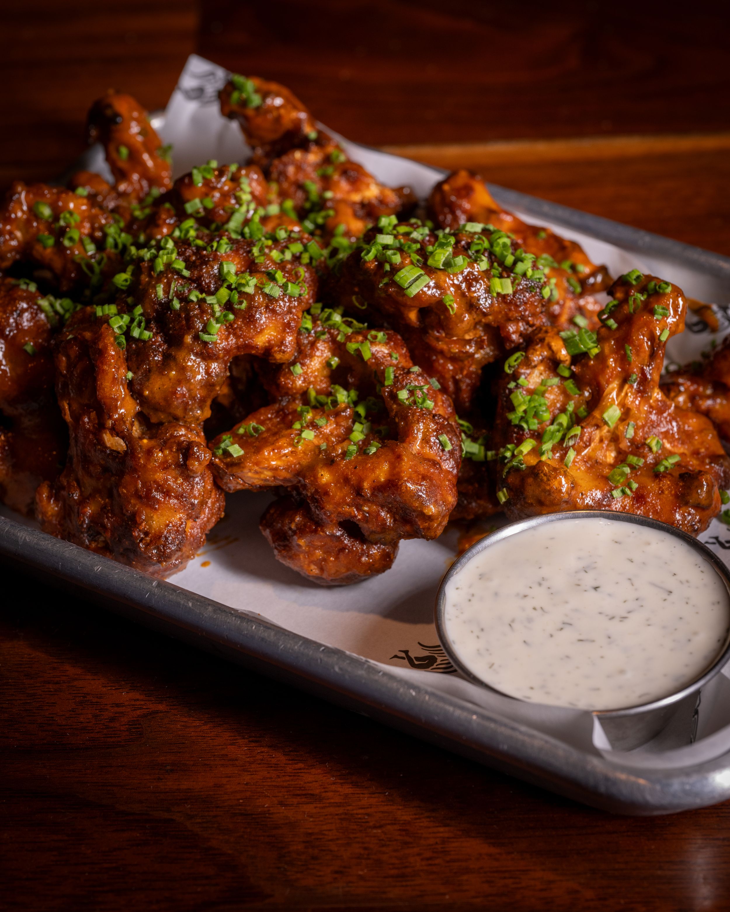 Crispy buffalo chicken wings glazed in tangy sauce, topped with fresh herbs, served with creamy ranch dip on a metal tray.