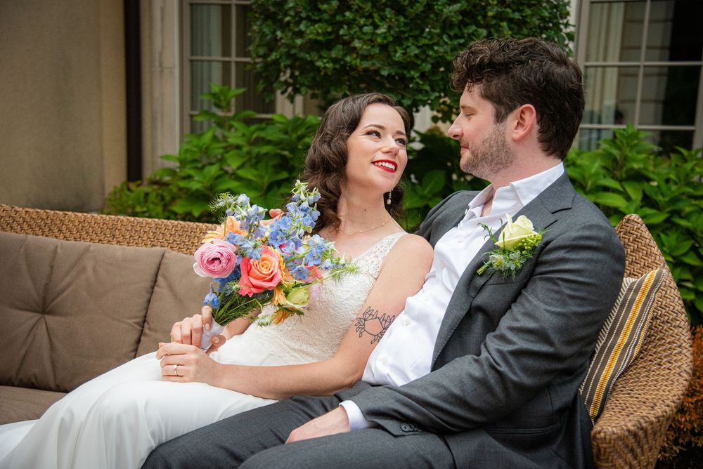 Elegant wedding couple relaxing on wicker furniture in garden setting.