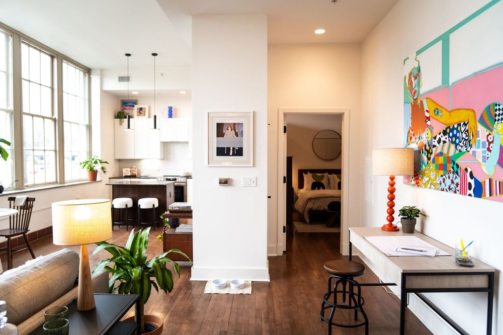 Modern open concept interior with white walls, hardwood floors, and large windows.
