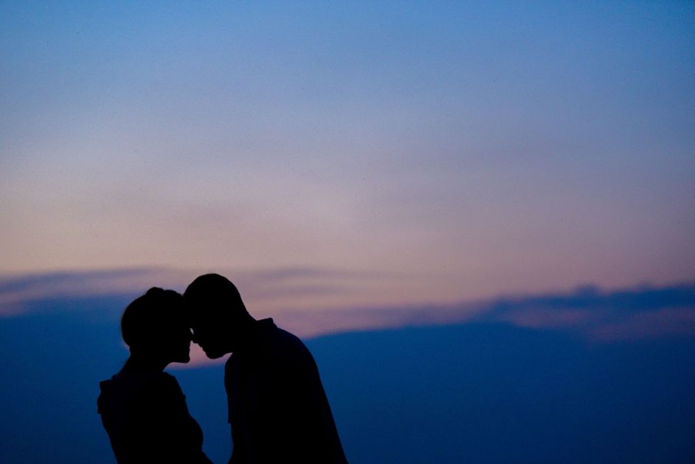 Silhouette of a romantic couple touching foreheads against a stunning purple and pink twilight sky.