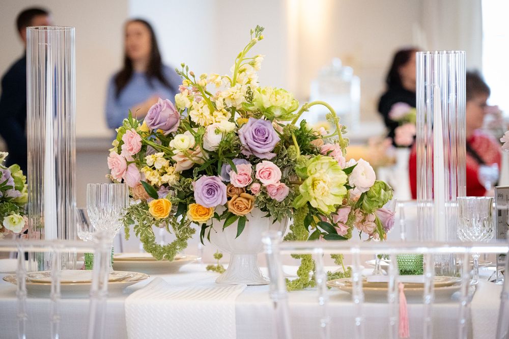 Elegant wedding table centerpiece with pastel roses, lavender blooms, and greenery in a white bowl vase.