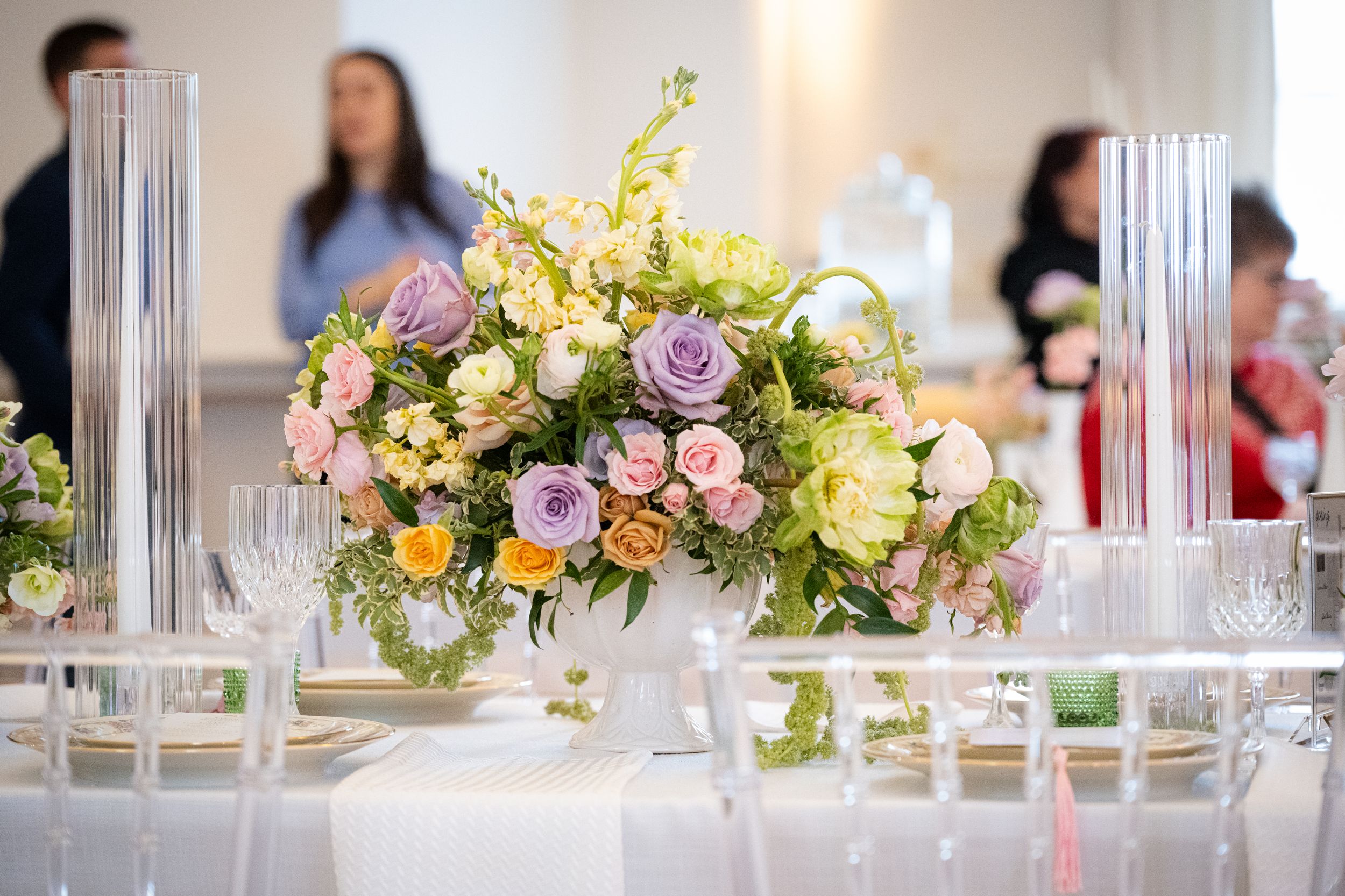 Elegant wedding table centerpiece with pastel roses, lavender blooms, and greenery in a white bowl vase.