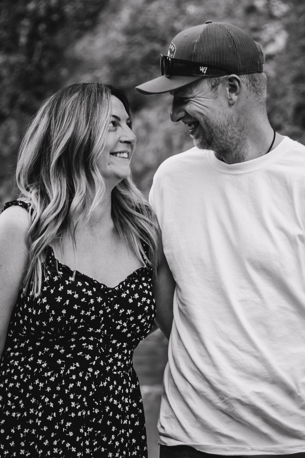 A romantic black and white portrait of a couple smiling at each other outdoors.