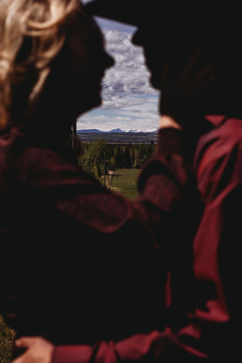 Couple silhouetted against mountain landscape view, framed by their profiles in romantic outdoor setting.