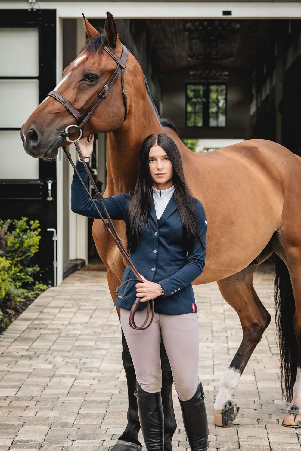 A female equestrian in riding attire stands beside a bay horse outside a stable. Equestrian Photographer, Photographer, Photography, Photo