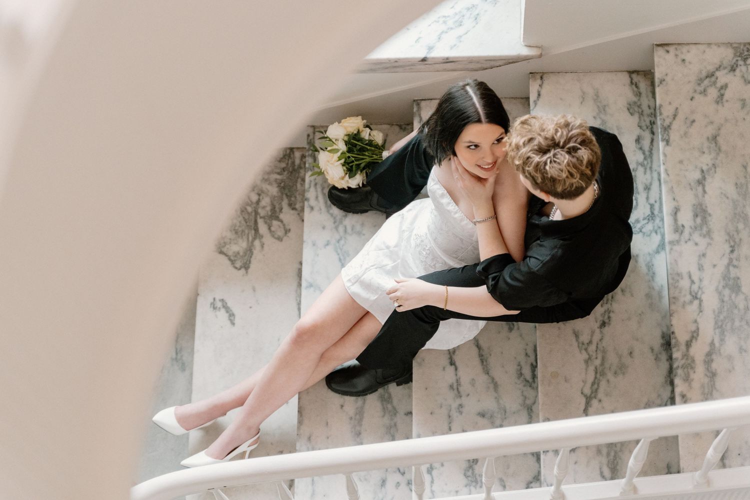 A lesbian couple sitting on courthouse stairs before their elopement
