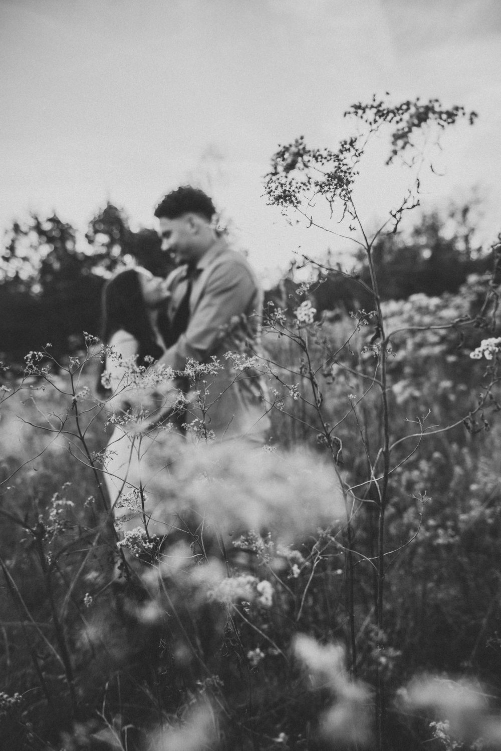Dreamy black and white photo of couple among wild flowers in meadow.
