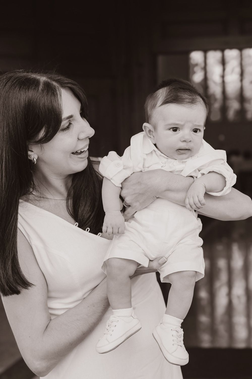 Black and white photo of a smiling woman holding an adorable baby dressed in white at what appears to be a christening.