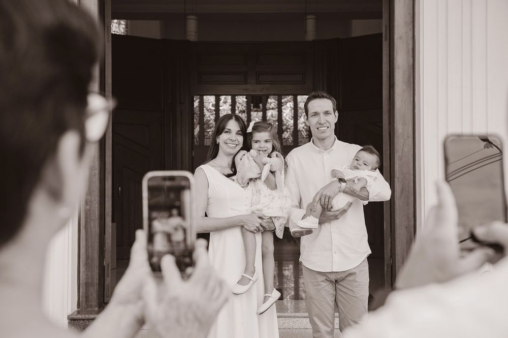 Black and white photo of a family with two children posing at a doorway while guests photograph them.