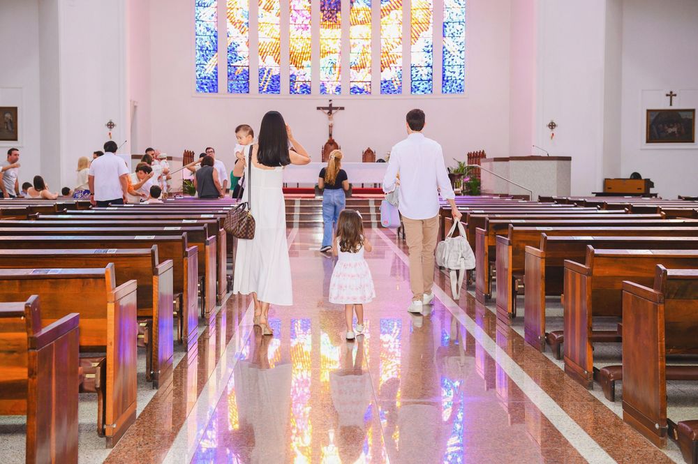 Family walking down church aisle toward altar during a religious ceremony, with wooden pews and stained glass windows.