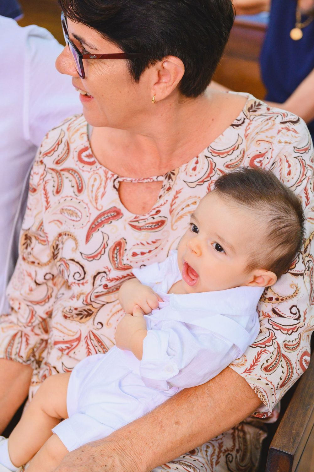 Grandmother holding a baby dressed in white at a christening ceremony.