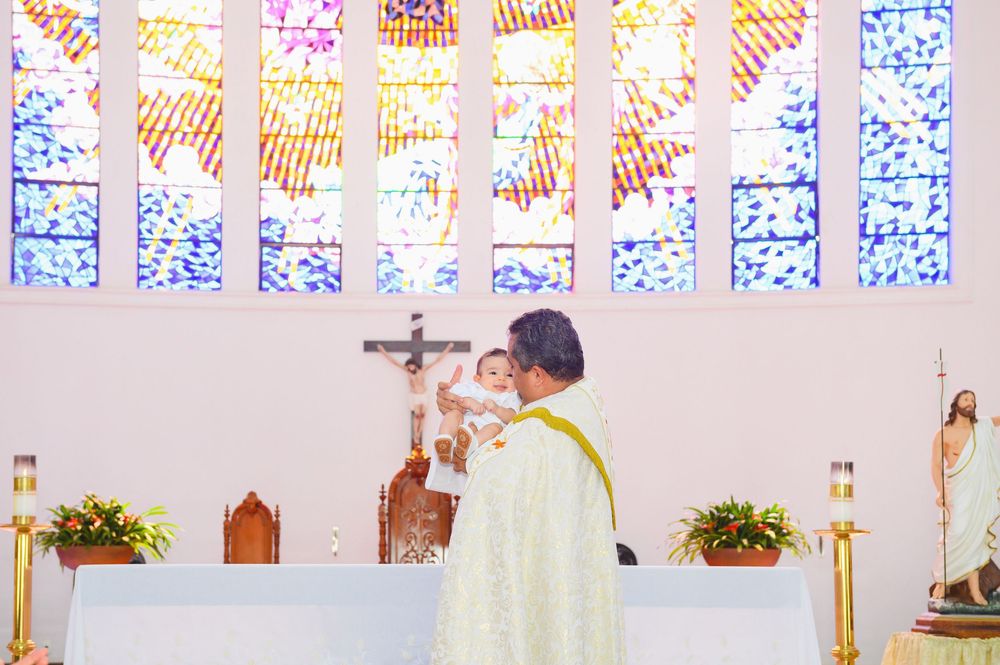 Priest elevating the Eucharist during Catholic Mass at a church altar with colorful stained glass windows.