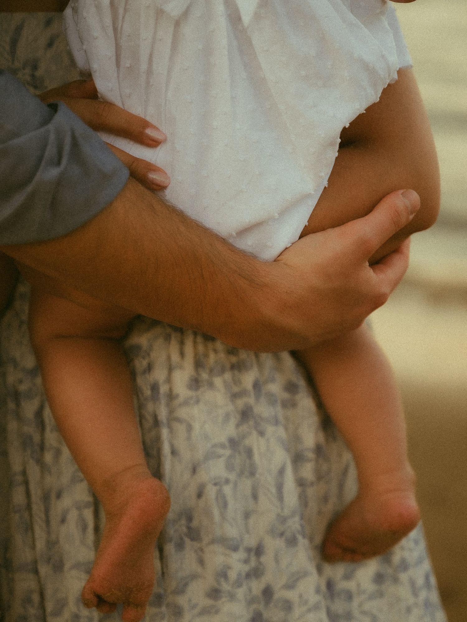 An adult carefully holds a small baby against their body, with the infant's tiny legs and feet visible.