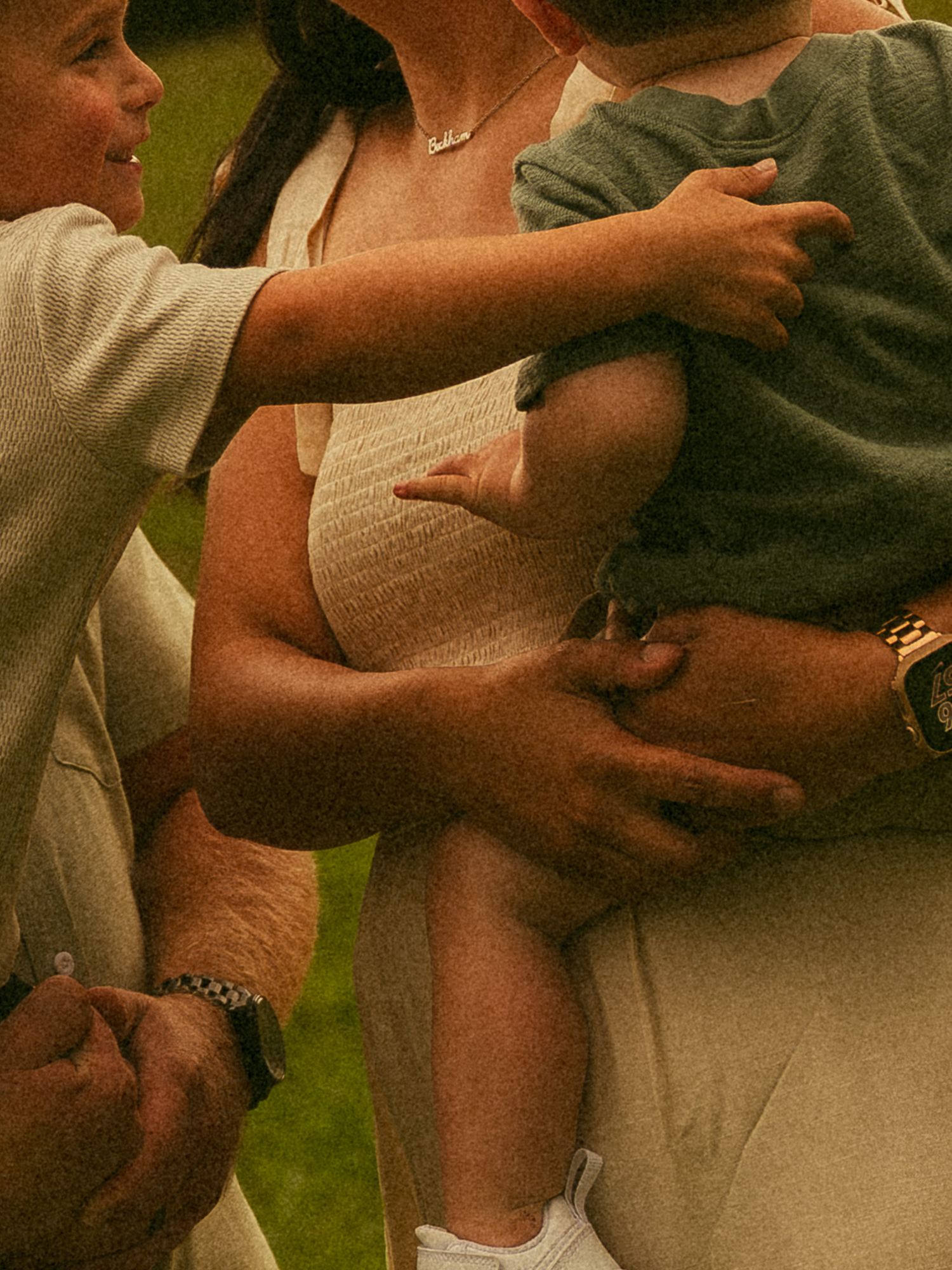 Adults holding a young child outdoors on a green lawn, wearing casual summer clothing.