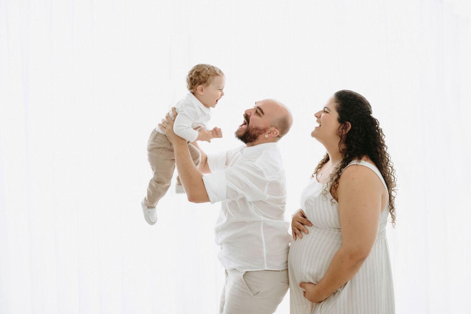 A mother in a striped dress holds her baby against a soft white background.