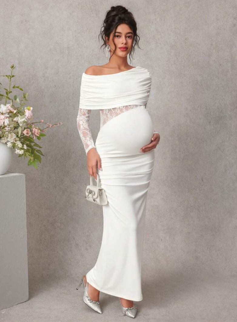 White off-shoulder maternity maxi dress with lace sleeves, ruched bodice, and fitted silhouette, styled with silver heels.