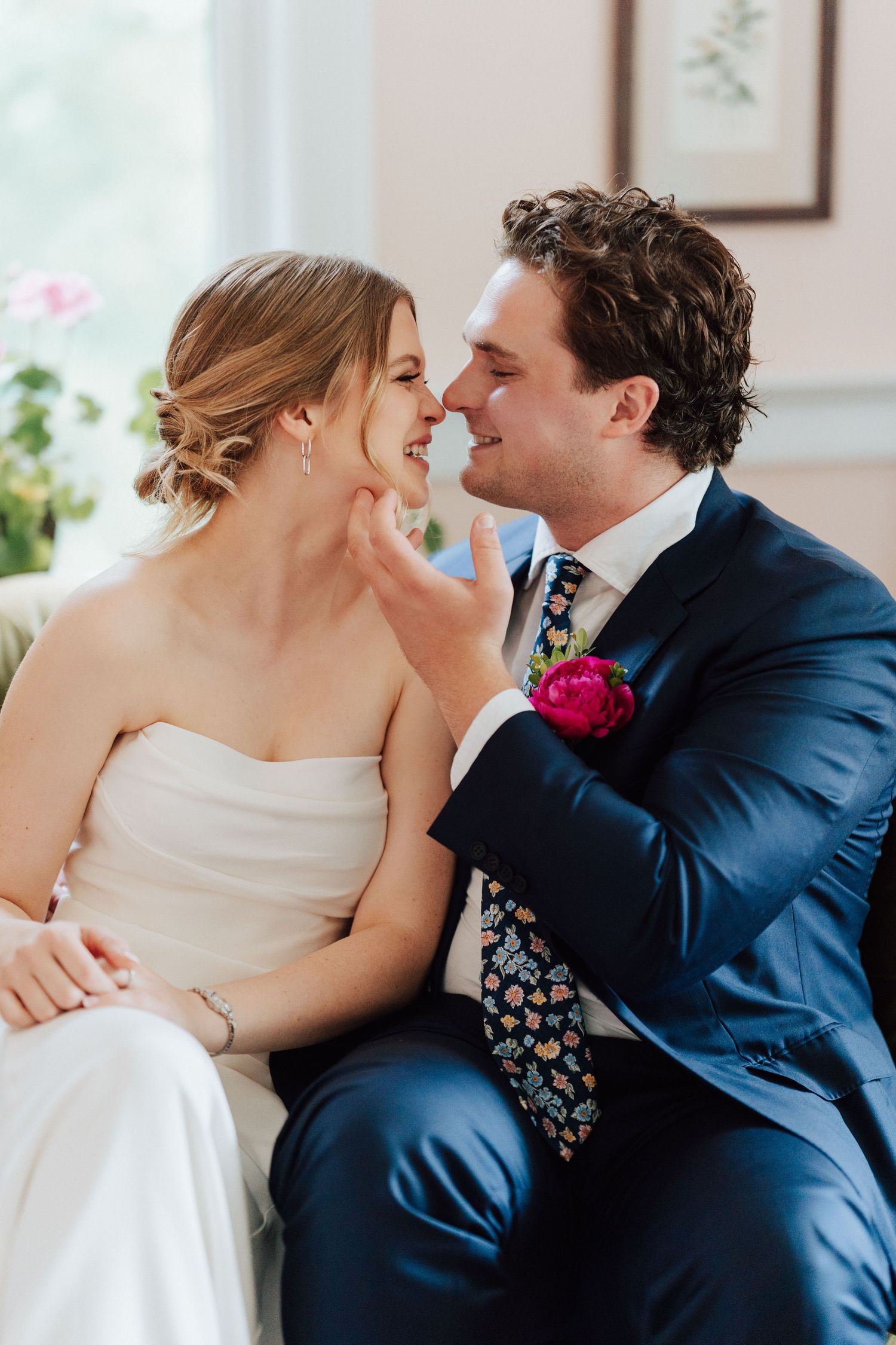 A joyful bride and groom share a tender moment, smiling face-to-face, as he gently cups her chin during their wedding day.