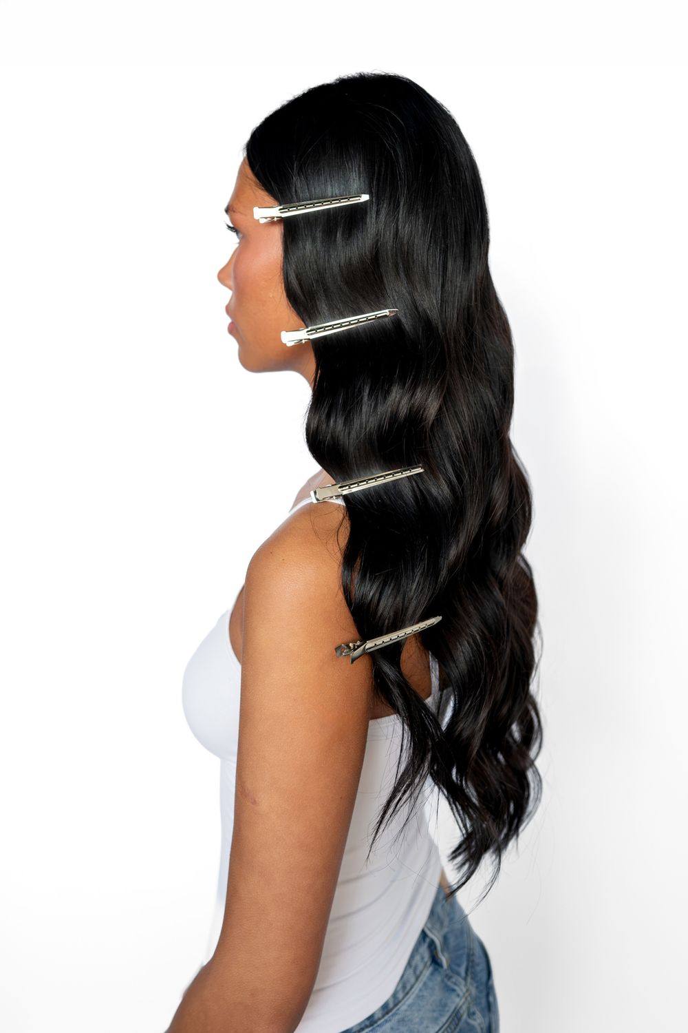 Woman with long wavy black hair styled with decorative silver hair clips, wearing a white top, side profile view.