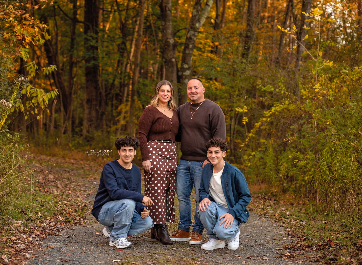 Family of four posing on a forest path surrounded by vibrant autumn foliage for a fall portrait session.