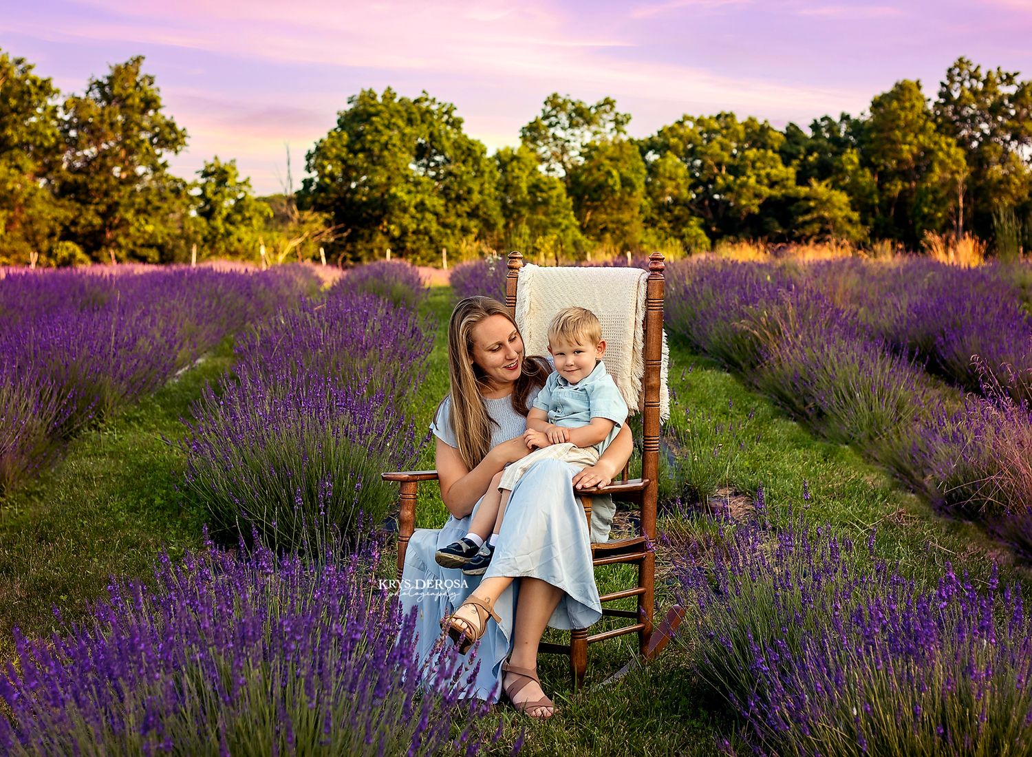 Mother and toddler sitting in a wooden chair surrounded by purple lavender fields at golden hour sunset.