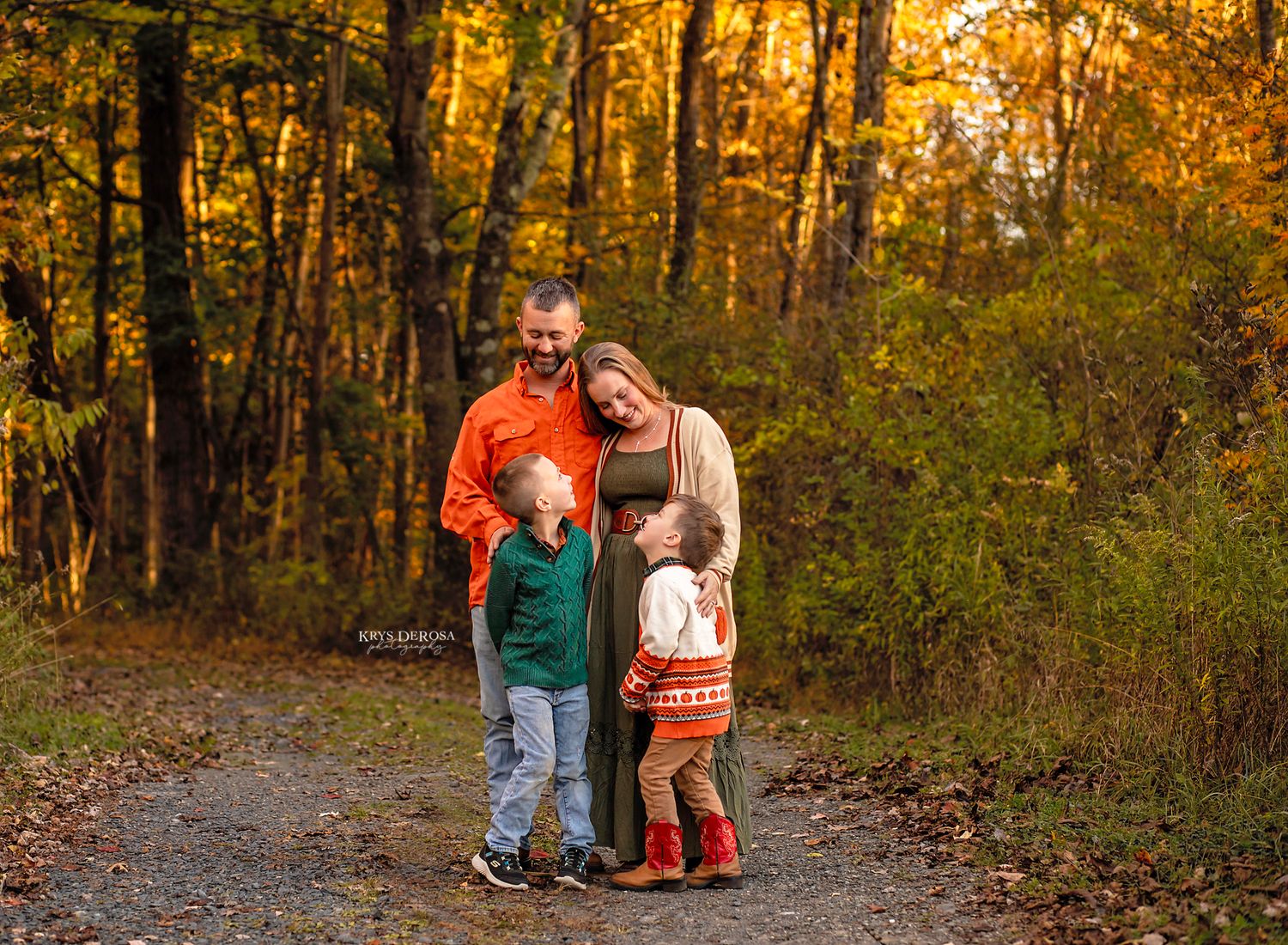 Family of four posing on autumn forest path surrounded by colorful fall foliage.