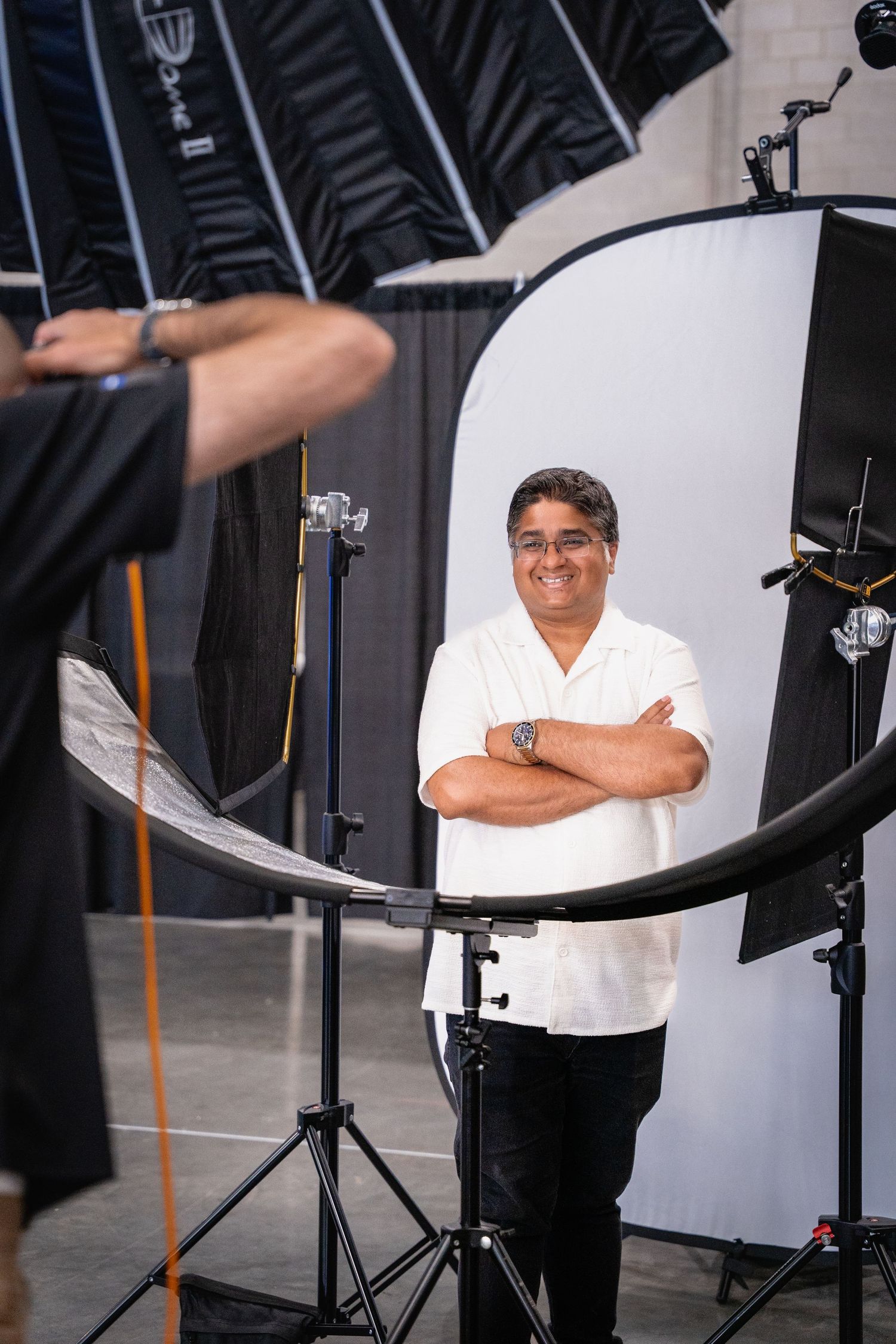 Man with crossed arms posing in a professional photo studio surrounded by lighting equipment and reflectors.