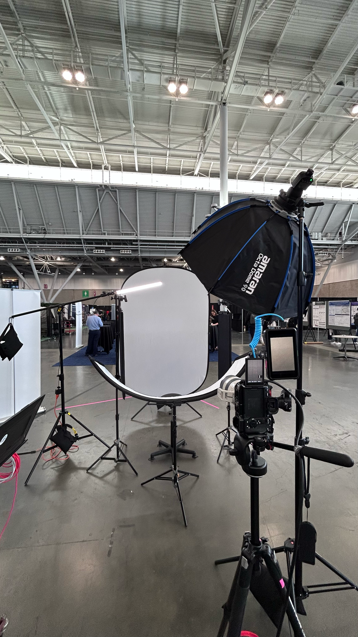 Professional photography studio setup with softboxes and light stands in a large convention center or exhibition hall.
