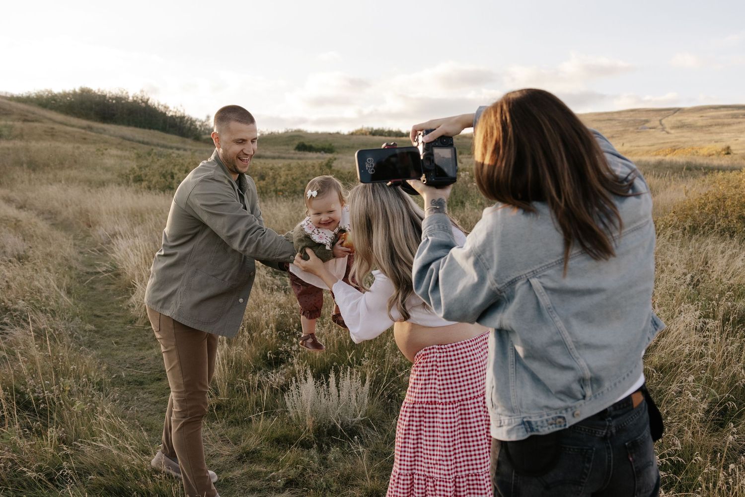 Photographer capturing a family portrait session in a scenic grassy valley with rolling hills in the background.