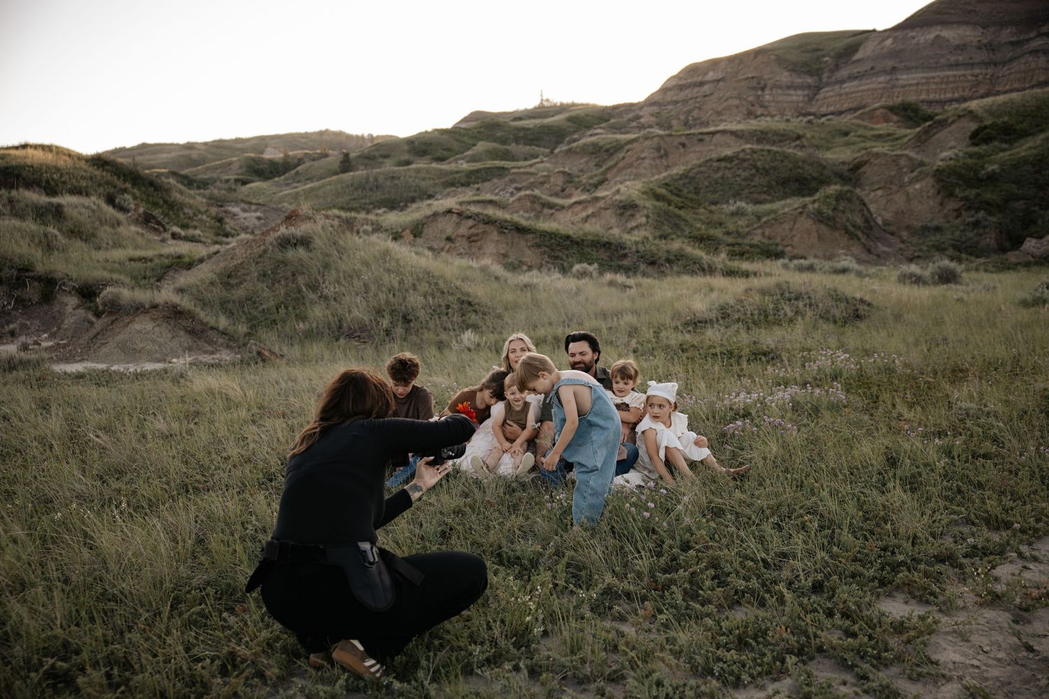 Photographer capturing a family portrait session in a scenic grassy valley with rolling hills in the background.