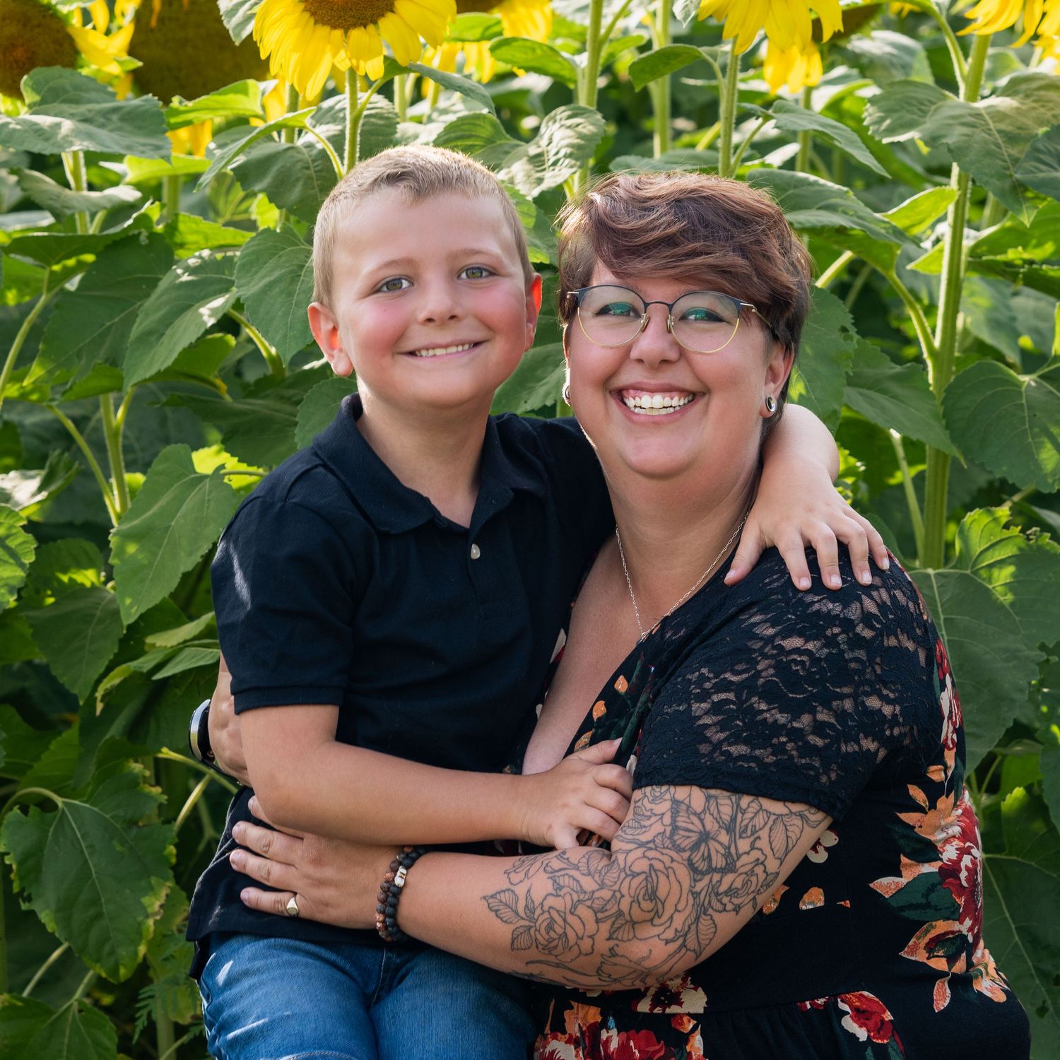 A smiling woman and young boy pose together in a vibrant sunflower field for New Hampshire sunflower mini sessions