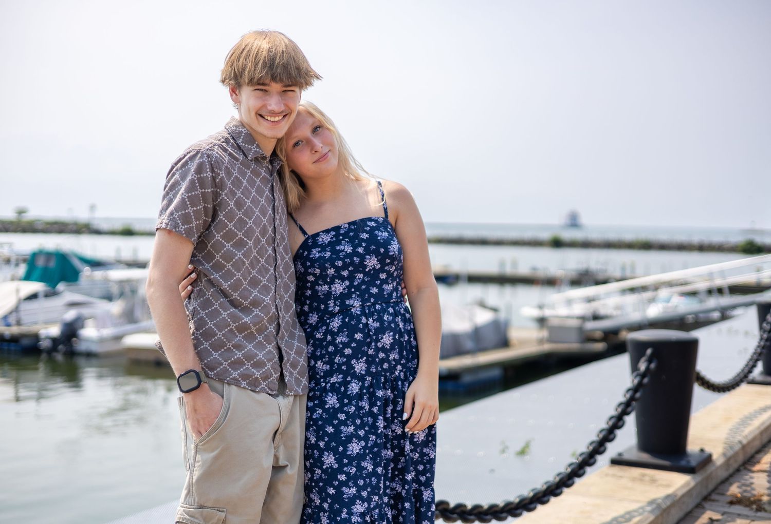 Young couple smiling and embracing on a marina dock with boats in the background.
