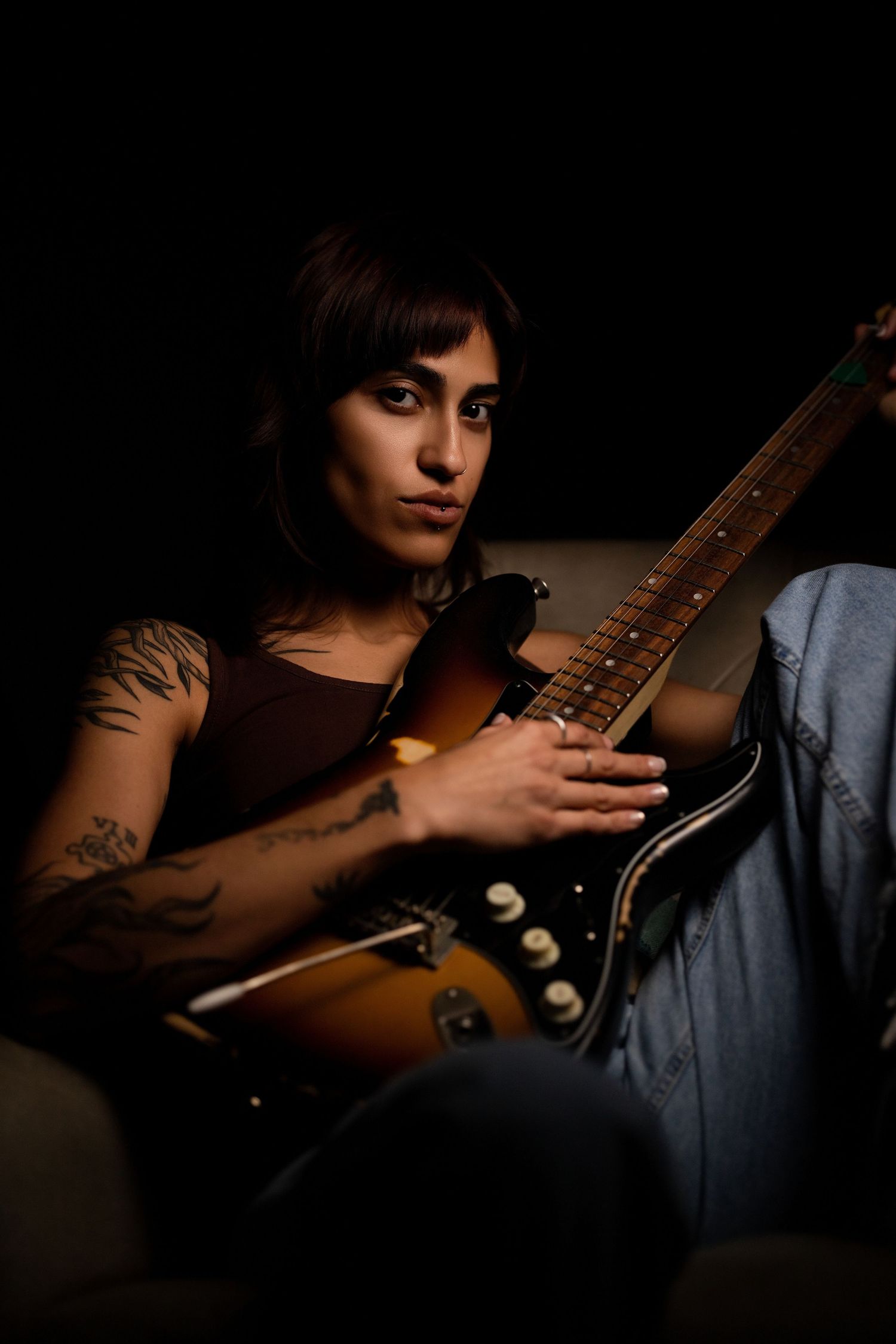 Tattooed woman playing electric guitar in dramatic low-key lighting.