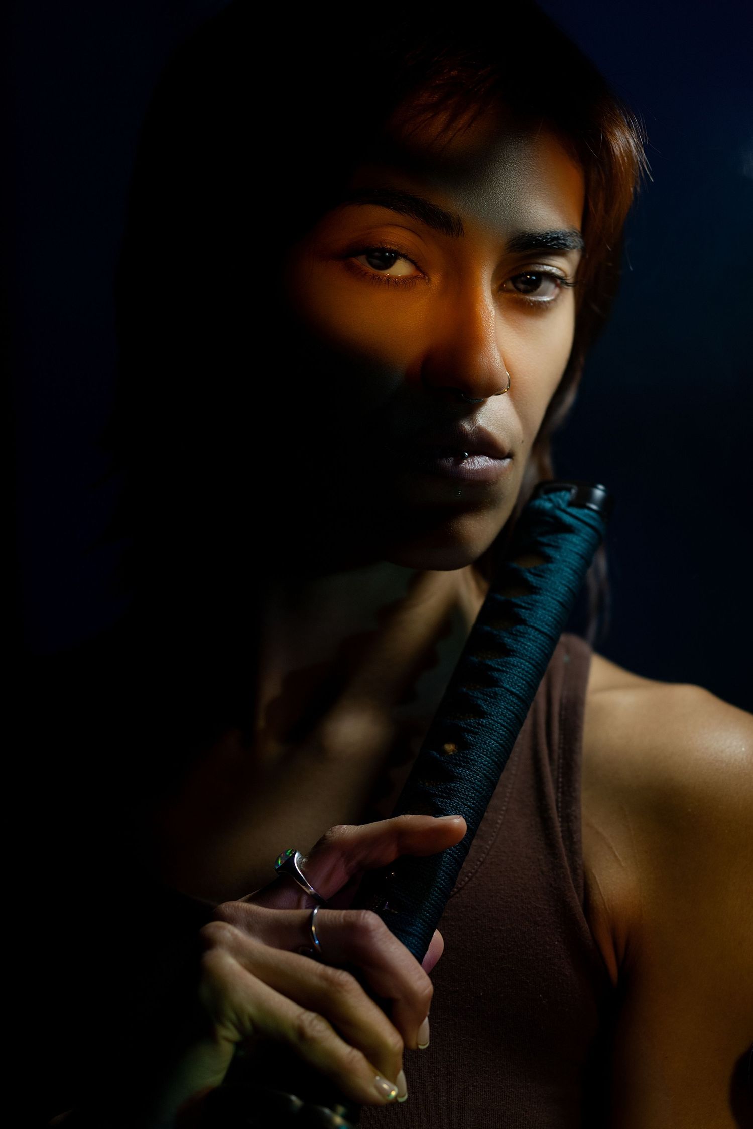 Intense portrait of woman holding katana in dramatic orange and blue light.