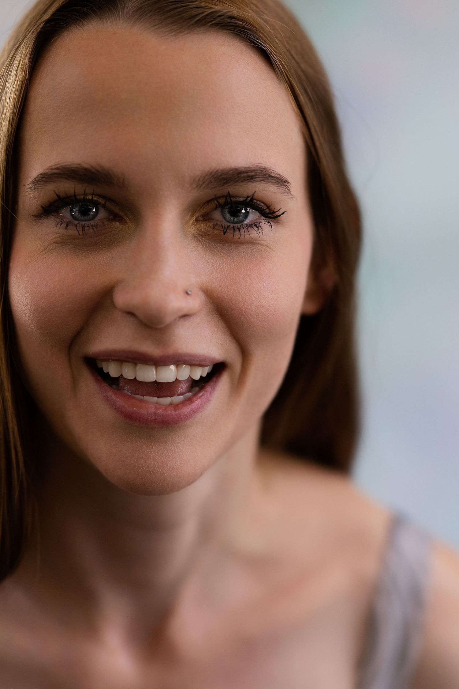 Smiling young woman with blue eyes and nose piercing in bright natural light.