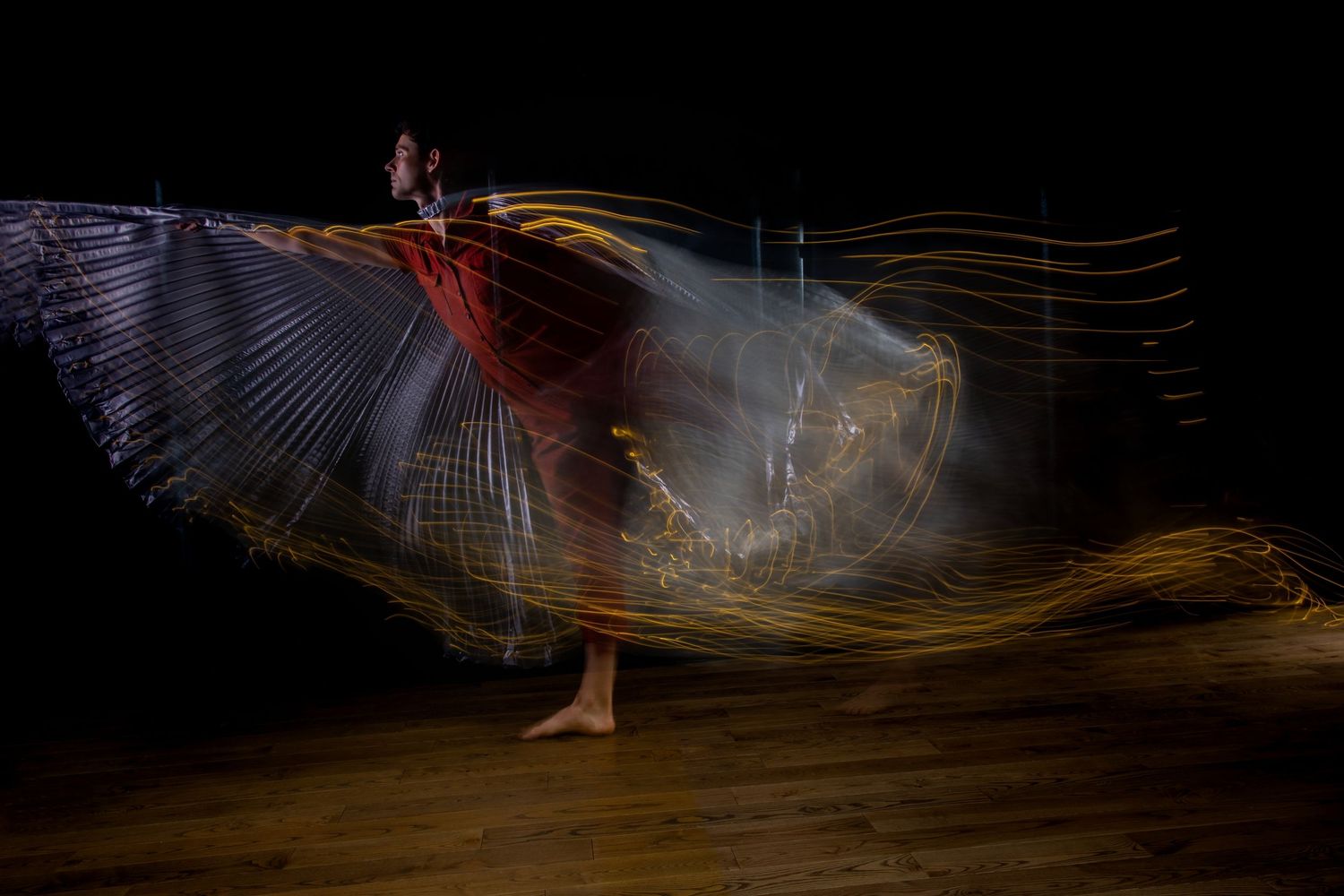 Long exposure dance performance with flowing wings and light trails on stage.