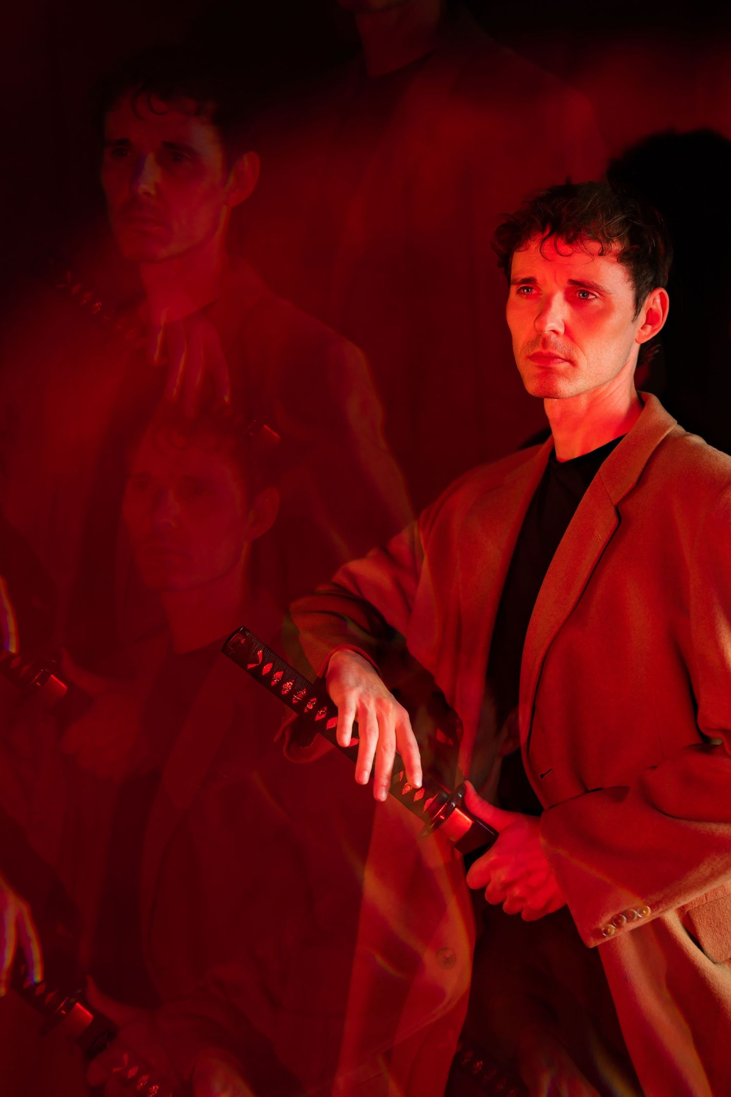 Man in beige blazer holding katana with red-tinted multiple exposure effect.