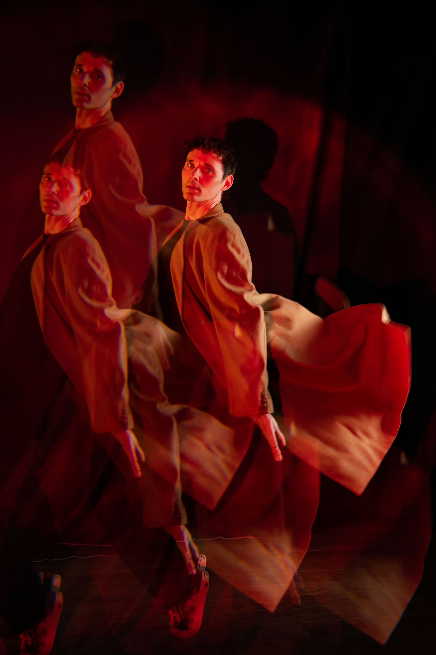Multiple exposure photo of a male dancer in red robes performing dynamic movements against dark background.