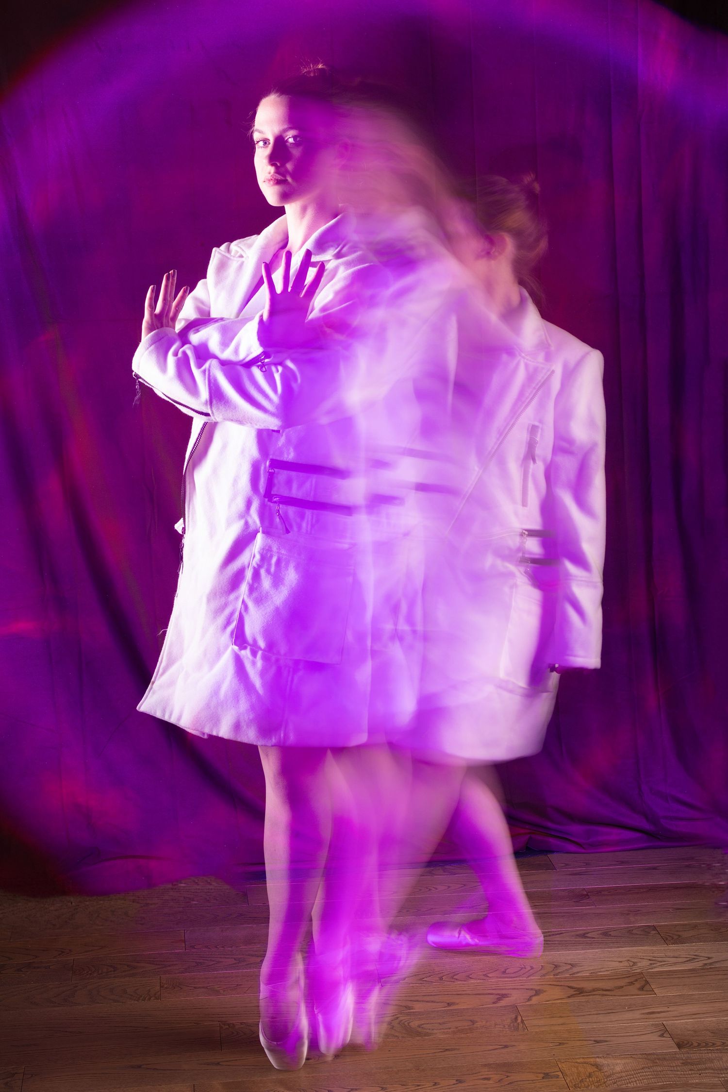 Long exposure photo of a woman in white lab coat with motion blur effect under purple lighting.