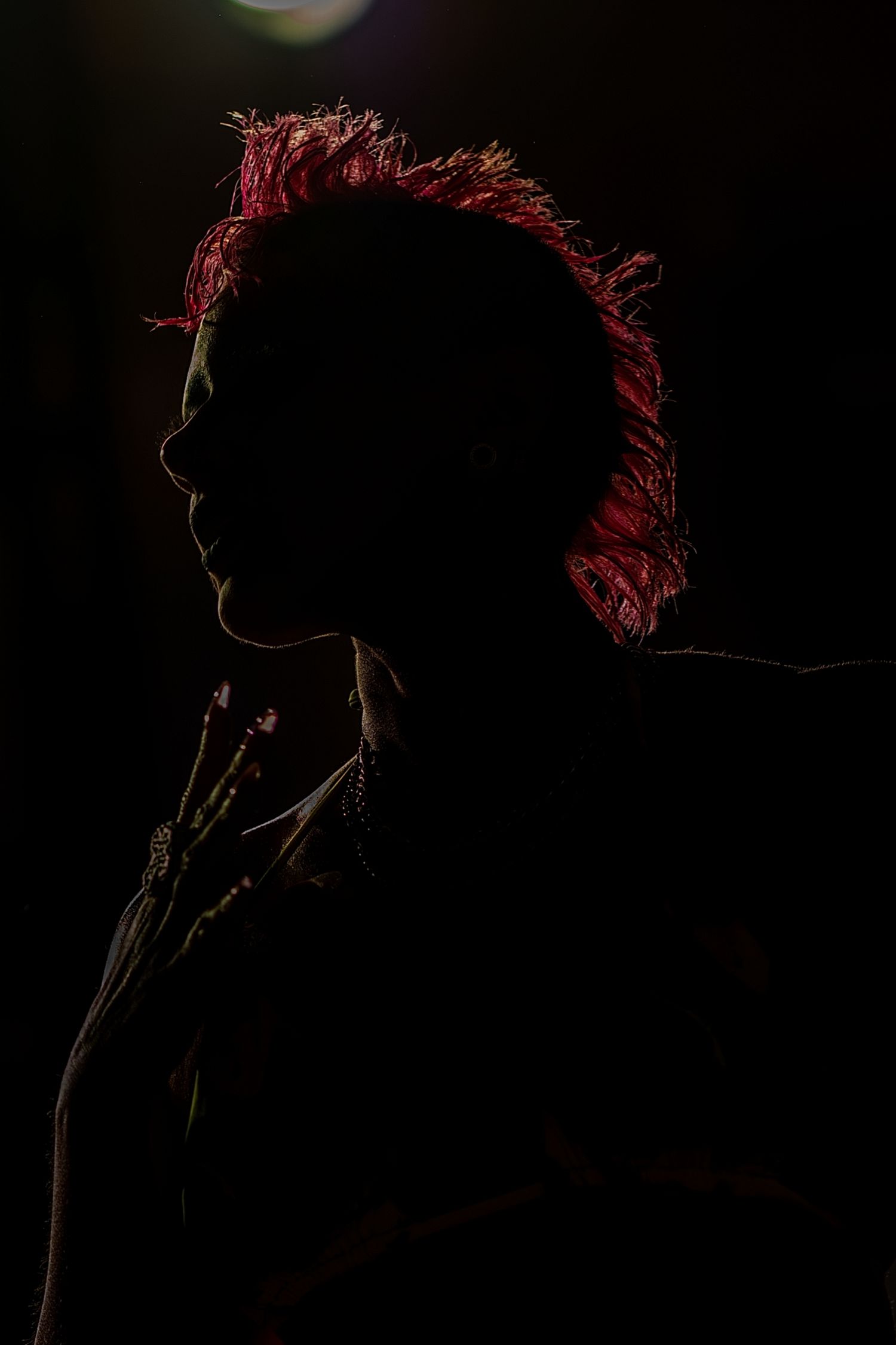 Dramatic silhouette profile of person with vivid red hair illuminated against black background.