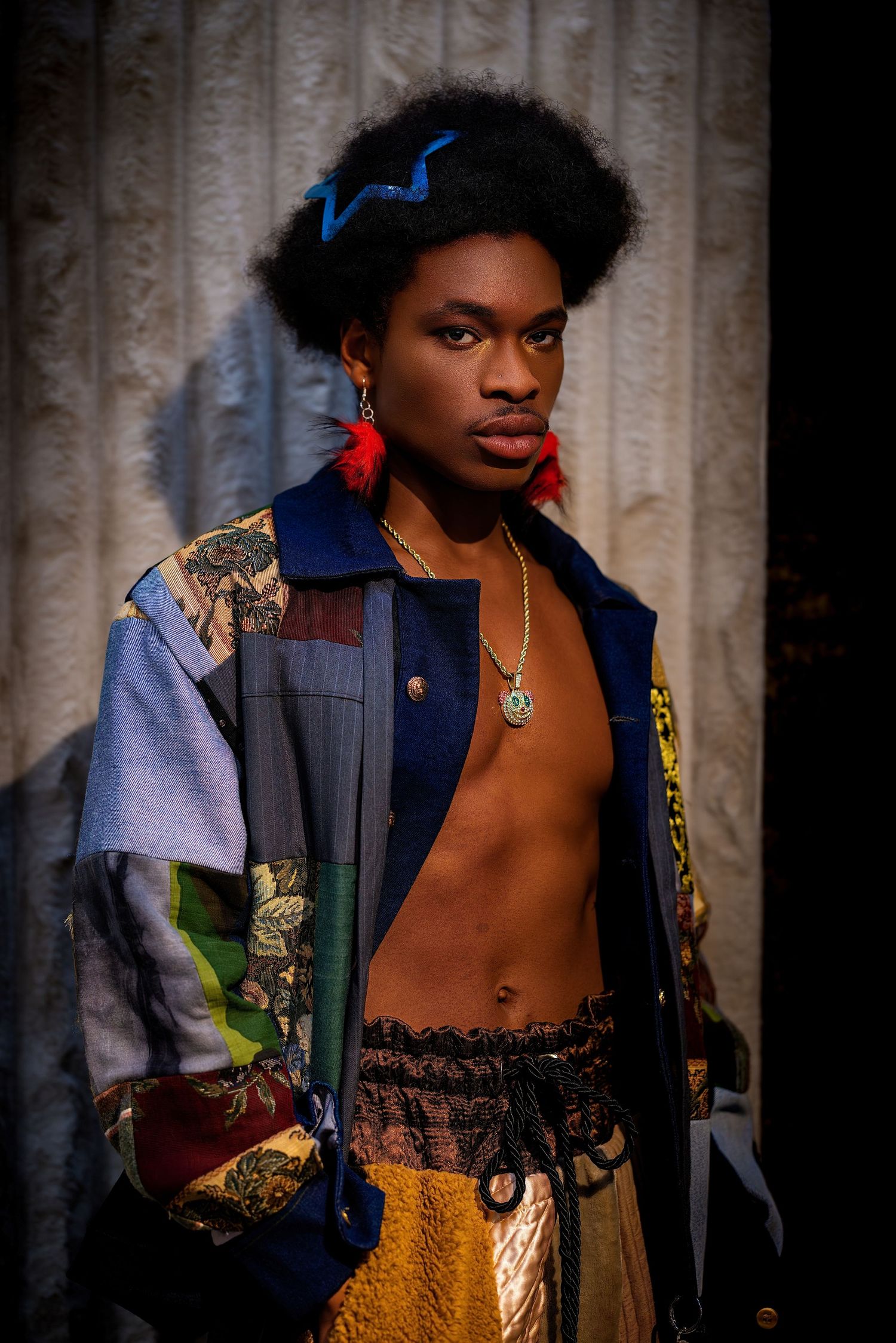 Fashion model in open patchwork jacket with red earrings and gold necklace poses dramatically.