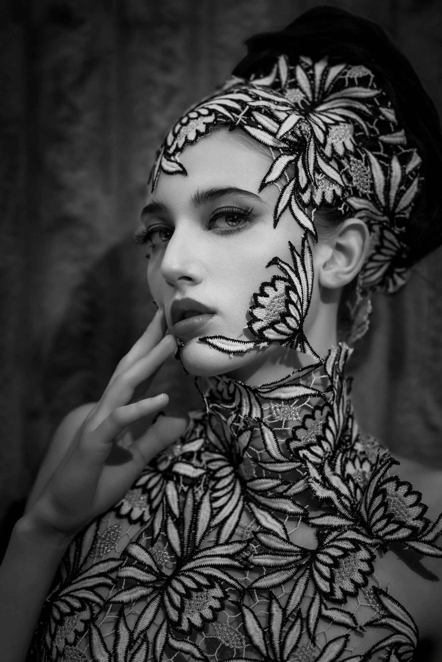 Black and white portrait of woman in elaborate floral lace bodysuit and matching headpiece.