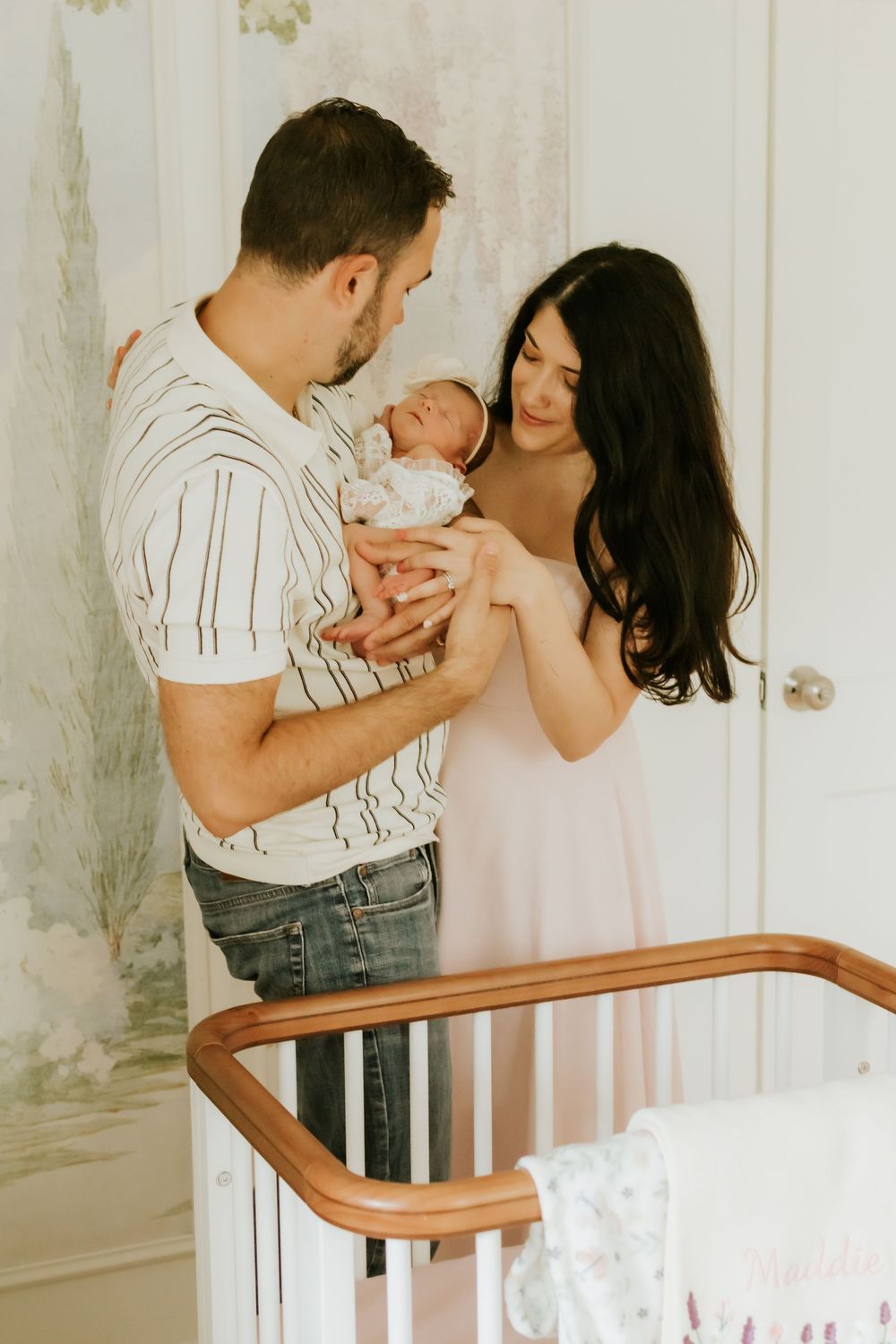 New parents lovingly hold their newborn baby together in a softly decorated nursery room.