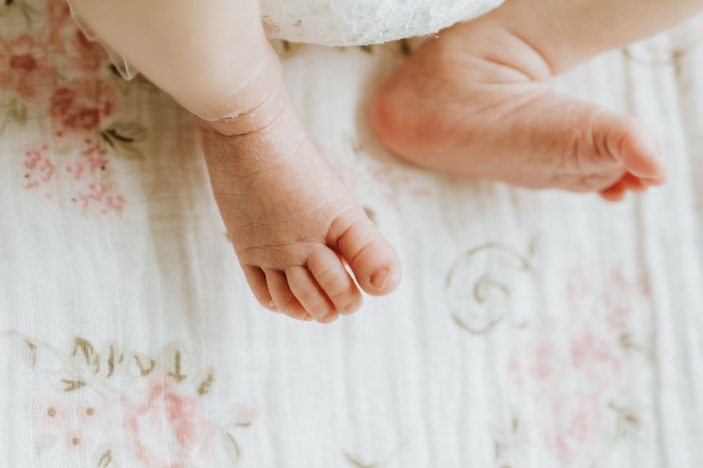 Close-up of tiny newborn baby feet resting on a soft white floral muslin blanket.