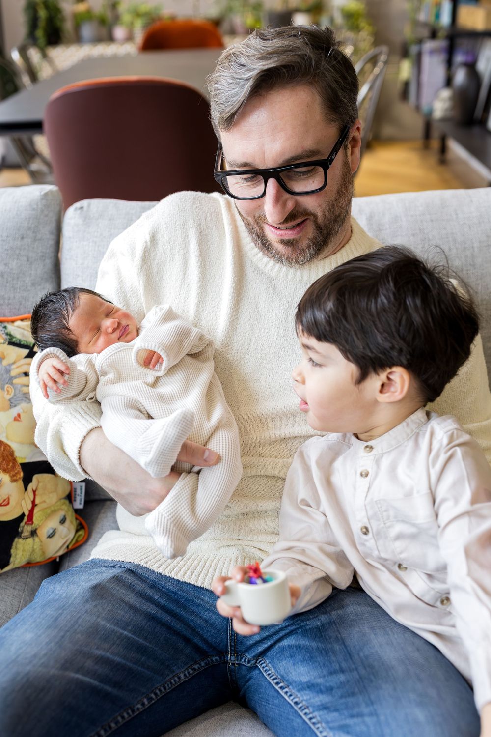 dad holding a baby in his arms while toddler looks on