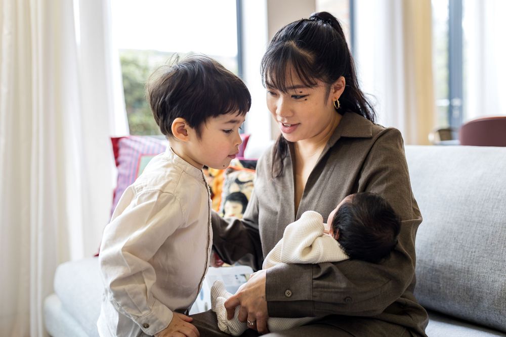 mum holding a newborn baby while older toddler looks on